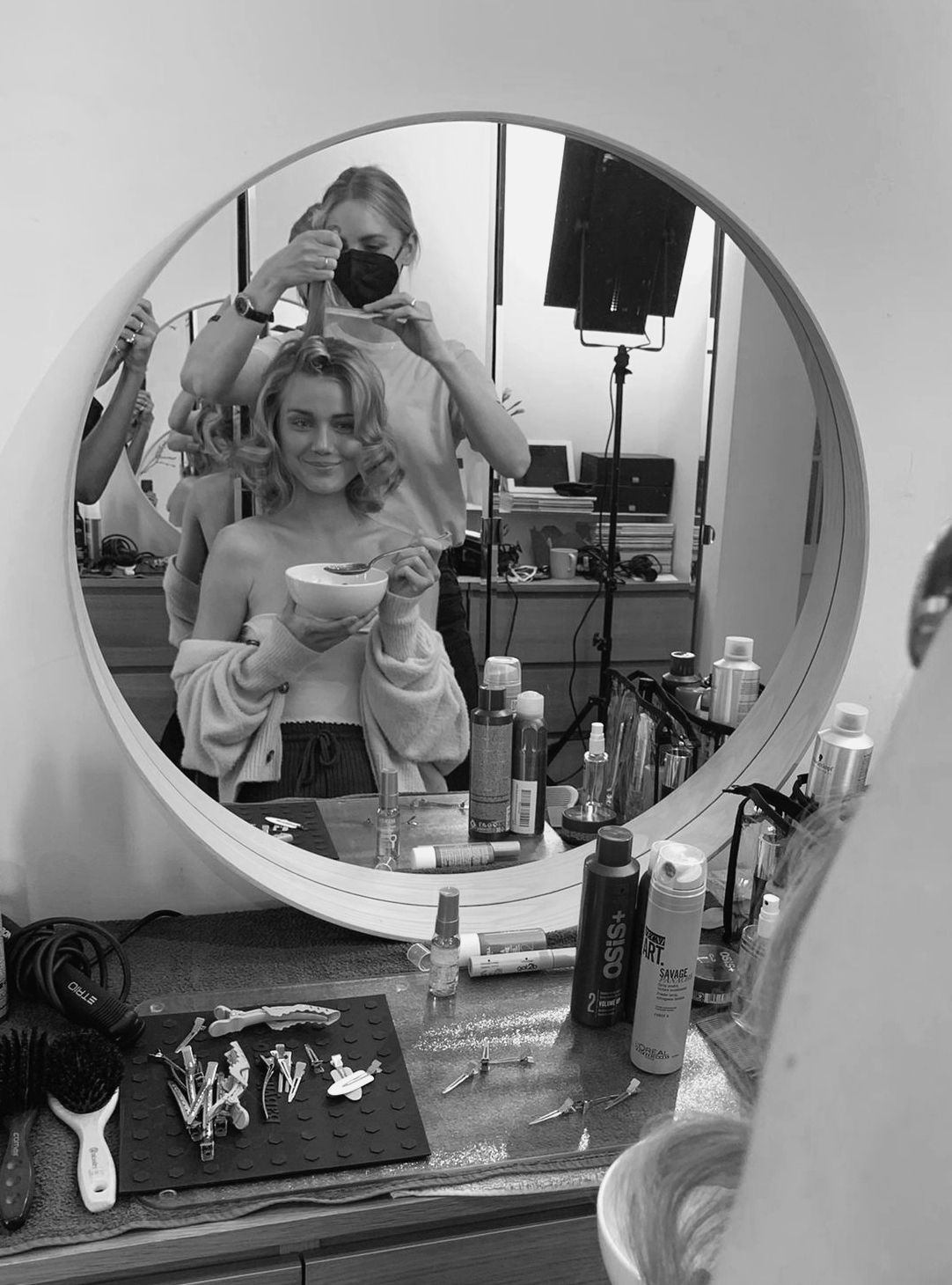 Hair & Make-up Artist Eva Gerholdt stylt die Haare eine Kundin, die den Styling-Vorgang entspannt und fröhlich über den Spiegel verfolgt